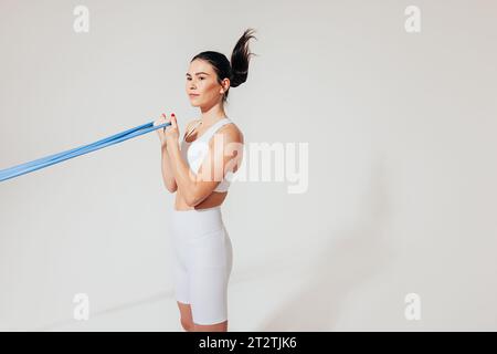 Seitenansicht einer schlanken Frau in weißer Fitnesskleidung, die Bizepscurl mit Widerstandsband macht Stockfoto