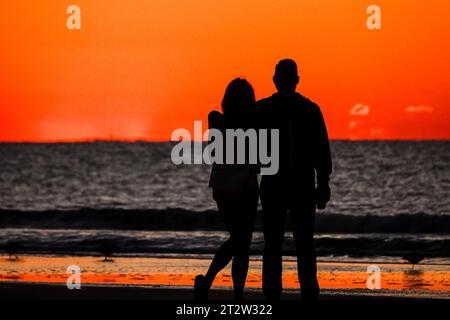 Isle Of Palms, Usa. Oktober 2023. Ein Paar mit einer Silhouette vom Sonnenaufgang, während sie beobachten, wie die Sonne am Horizont des Atlantischen Ozeans von Front Beach aus kommt, 21. Oktober 2023 in Isle of Palms, South Carolina. Quelle: Richard Ellis/Richard Ellis/Alamy Live News Stockfoto