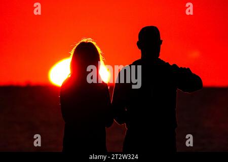 Isle Of Palms, Usa. Oktober 2023. Ein Paar mit einer Silhouette vom Sonnenaufgang, während sie beobachten, wie die Sonne am Horizont des Atlantischen Ozeans von Front Beach aus kommt, 21. Oktober 2023 in Isle of Palms, South Carolina. Quelle: Richard Ellis/Richard Ellis/Alamy Live News Stockfoto