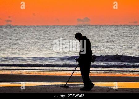 Isle Of Palms, Usa. Oktober 2023. Ein Metalldetektor mit der Silhouette des Sonnenaufgangs sucht am Front Beach, 21. Oktober 2023 in Isle of Palms, South Carolina, nach Gegenständen, die von Sonnenanbetern zurückgelassen wurden. Quelle: Richard Ellis/Richard Ellis/Alamy Live News Stockfoto