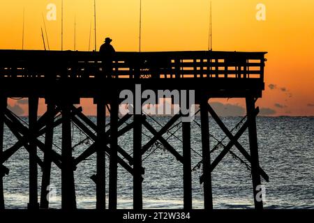 Isle Of Palms, Usa. Oktober 2023. Ein Fischer, der von Sonnenaufgang umgeben ist, wartet auf einen Fang am Isle of Palms Pier, 21. Oktober 2023 in Isle of Palms, South Carolina. Quelle: Richard Ellis/Richard Ellis/Alamy Live News Stockfoto