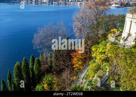 Fantastischer alter Park neben dem Wasser des Luganer Sees - Herbstblattfarbe. Und am Ufer der Stadt Lugano in der Ferne Stockfoto