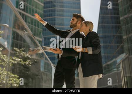 Geschäftsmann zeigt seiner Kollegin etwas, während er mit Laptop auf der Büroterrasse steht Stockfoto