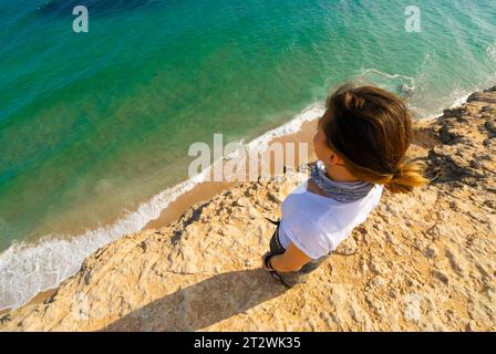 Eine Frau steht am Rande einer Klippe mit Blick auf das Meer in Oman Stockfoto