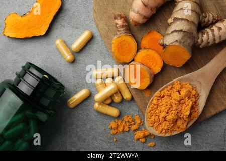 Aromatisches Kurkumapulver, Pillen und rohe Wurzeln auf grauem Tisch, flach gelegt Stockfoto