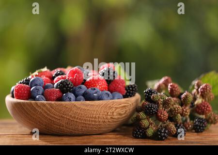 Schüssel mit verschiedenen frischen Beeren auf Holztisch im Freien Stockfoto