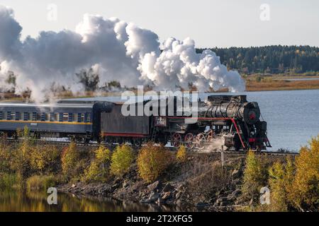 HELYULYA, RUSSLAND - 06. OKTOBER 2023: Dampflokomotive L-5164 mit Retro-Zug 'Ruskeala Express' auf dem Staudamm des Kalmaranyarvi-Sees an einem Oktobertag, Ka Stockfoto