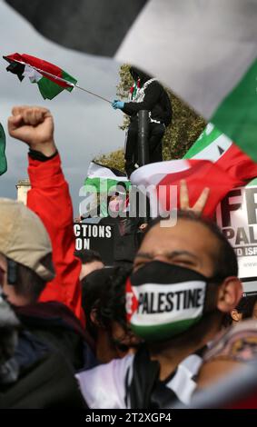 Pro-palästinensische Demonstranten versammeln sich, um Unterstützungsreden vor der Downing Street zu hören. Man steigt an einer Ampel und schwenkt eine palästinensische Flagge. Anhänger Palästinas kommen zusammen, um nach dem israelischen Bombenanschlag und der drohenden Bodeninvasion israelischer Truppen in Gaza in die Downing Street zu marschieren. Dies ist die zweite Woche in Folge, in der über 100.000 Menschen auf die Straßen Londons gingen, um zu protestieren. Viele der beteiligten Organisationen rufen allgemein dazu auf, einen Waffenstillstand, die Öffnung des Übergangs Rafah nach Ägypten und humanitäre Hilfe in den Gazastreifen zu ermöglichen. Stockfoto