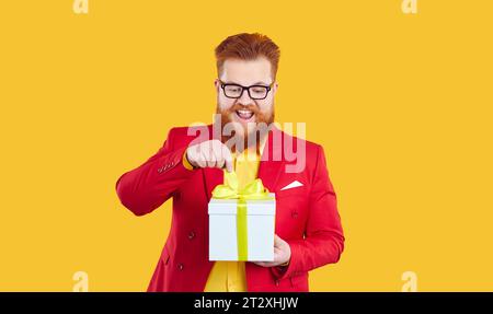 Lustiger, glücklicher, aufgeregter bärtiger fette Mann öffnet Geschenkbox isoliert auf lebhaftem gelbem Hintergrund. Stockfoto