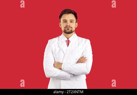 Herrenmode. Porträt eines hübschen brünetten Mannes in elegantem klassischem Anzug auf rotem Hintergrund steht mit überkreuzten Armen. Kopierbereich Stockfoto