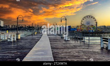 Hölzerne Promenade bei Sonnenuntergang unter einem orangefarbenen Himmel am berühmten Santa Monica Pier mit seinem Riesenrad in der Nähe der Stadt Los Angeles im Bundesstaat Cali Stockfoto