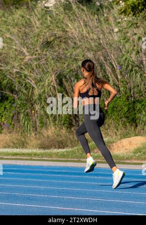 Schönes junges, schlankes, gebräuntes Läufermädchen, in enger Sportbekleidung gekleidet, mit Stil und perfekten technischen Laufbewegungen, die seitlich auf einem laufen Stockfoto