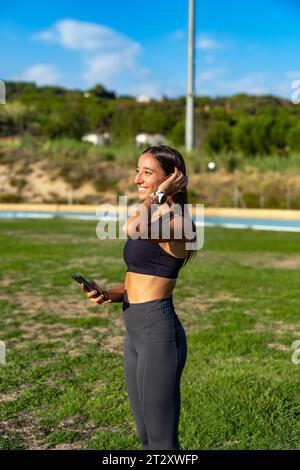 Schöne junge schlanke Läuferin, sehr glücklich und lächelnd, berührte ihr langes Haar, schaute in die Ferne auf einen Bekannten oder Freund in einer Leichtathletik Stockfoto