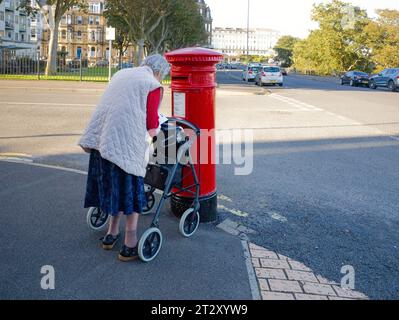 Eine ältere Frau mit Gehhilfe, die Briefe in einen viktorianischen Briefkasten in Scarborough postet Stockfoto