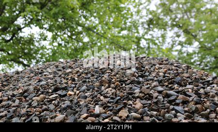 Blick von unten auf einen Berg aus grauem Kies auf einem verschwommenen Hintergrund aus grünem Laub, Landschaftsdetails mit kleinem Felsen, der auf einem bröckeligen Haufen liegt Stockfoto