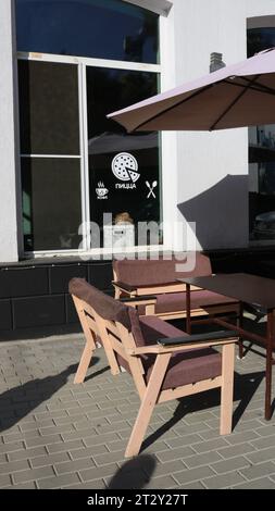 pizzeria mit Außentischen und Sonnenschirmen, die neben dem Fenster stehen, mit Aufschriften in russischer „Kaffee“ und „Pizza“, straßencafé in einer Stadt Stockfoto