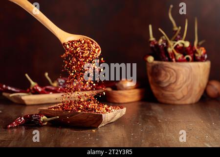 Chiliflocken werden in eine Holzschale gegossen. Chiliflocken und getrocknete Chilischoten auf einem alten Holztisch. Stockfoto