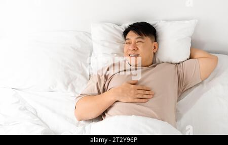 Ein Glücklicher Asiatischer Mann Mittleren Alters, Der Im Bett Liegt Stockfoto