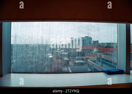 Glasfenster mit Regenwasserspuren mit trüben hohen Gebäudekulissen Stockfoto