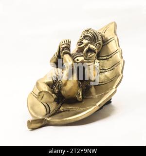 hindu-Gott-Lord Baby krishna auf einer Blattstatue, die detailliert auf glänzendem goldfarbenem Metall isoliert ist Stockfoto