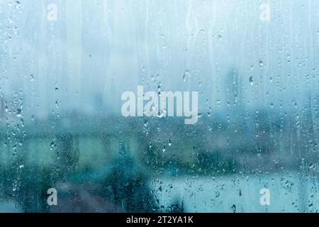 Glasfenster mit Regenwasserspuren mit trüben hohen Gebäudekulissen Stockfoto