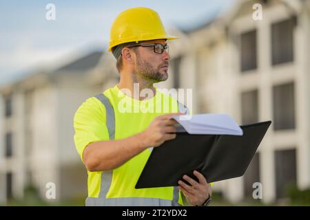 Ingenieur mit Klemmbrett, Gebäudeinspektion. Bauarbeiter vor Ort. Arbeiter mit Schutzhelm. Bauarbeiter im Helm bei Neubau Stockfoto