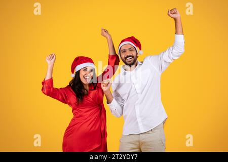 Fröhlicher lateinamerikanischer Mann und Frau in Santa-Hüten, feiert Feiertage mit erhobenen Händen, festlichem Beifall und Aufregung, Tanz Stockfoto