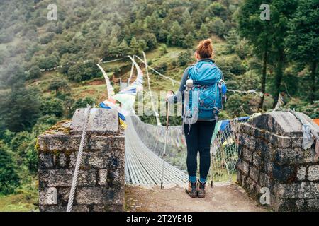 Junge Frauen überqueren den Canyon über die Hängebrücke mit bunten Tibetischen Gebetsfahnen, die über der Schlucht hängen. Wanderung auf dem Mera Gipfel bei Lukla Stockfoto