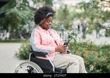 Afroamerikanische Frau mit Behinderung, die ihr Smartphone benutzt, um draußen online zu kommunizieren Stockfoto