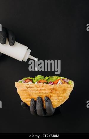 Kocht mit der Hand Soße in Döner-Döner durch gerissene Löcher auf schwarzem Papierhintergrund. Street Food Stockfoto