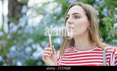 Junge blonde Frau, die Vaper im Park raucht Stockfoto