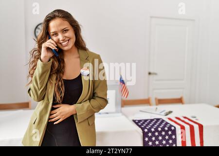 Junge, wunderschöne hispanische Frau, Wahlpräsidentin, die auf dem Wahlcollege mit einem Smartphone spricht Stockfoto