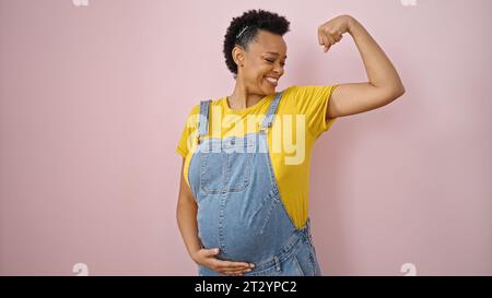 Junge schwangere Frau, die selbstbewusst lächelt und eine starke Geste auf isoliertem pinkfarbenen Hintergrund macht Stockfoto