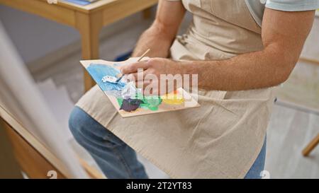 Junger hispanischer Künstler, der im Kunststudio Farbe auf Palette mischt Stockfoto