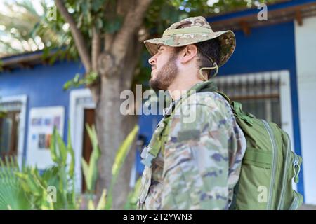 Junger hispanischer Mann in Tarnarmeeuniform im Freien mit Blick auf die Seite, entspannte Profilposition mit natürlichem Gesicht mit selbstbewusstem Lächeln. Stockfoto