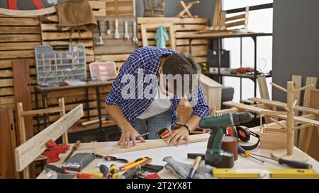 Gutaussehender junger arabischer Mann, ein professioneller Zimmermann, konzentrierte sich darauf, eine Markierung auf eine Holzdiele zu zeichnen, voll vertieft in seine Tischlerei im Arbeitsraum Stockfoto