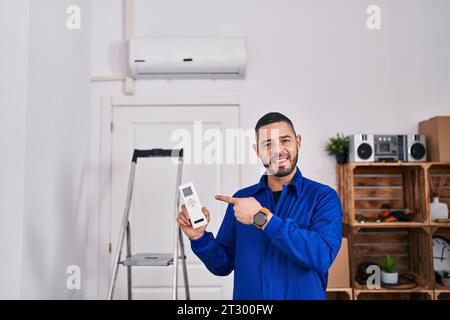 Hispanischer Servicemitarbeiter, der mit der Klimaanlage arbeitet, lächelte glücklich und zeigte mit Hand und Finger Stockfoto