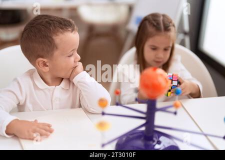 Ein süßes Mädchen und ein Junge, die mit einem Farbrätselwürfel spielen und im Kindergarten auf dem Tisch sitzen Stockfoto