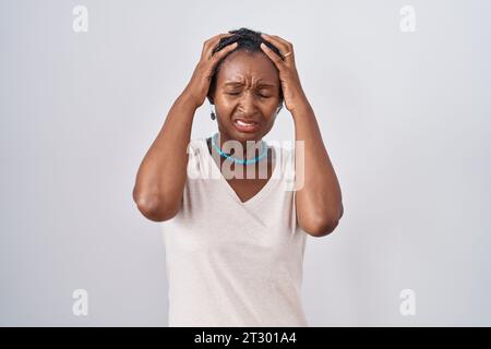 Afrikanische Frau mit Dreadlocks, die über weißem Hintergrund stehen und unter Kopfschmerzen leiden, verzweifelt und gestresst wegen Schmerzen und Migräne. Hände auf den Kopf. Stockfoto