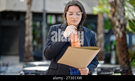 Junge, schöne hispanische Geschäftsfrau, die Dokumente auf der Terrasse des Cafés gestresst hält Stockfoto