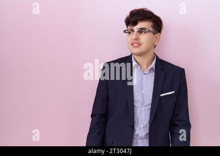Junger nicht binärer Mann mit Bart, Anzug und Krawatte, der mit einem Lächeln im Gesicht zur Seite blickt, natürlicher Ausdruck. Lacht selbstbewusst. Stockfoto