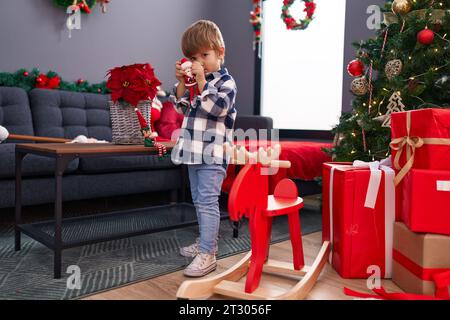 Entzückender hispanischer Junge, der zu Hause am weihnachtsbaum sitzt und ein Geschenk auspackt Stockfoto