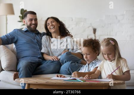 Fröhliche junge Eltern, die sich auf der Couch in einem gemütlichen Zuhause ausruhen Stockfoto