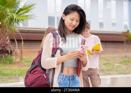 Glückliche junge asiatische Frau, die im Internet mit einem mobilen Gerät im Freien surft. Stockfoto