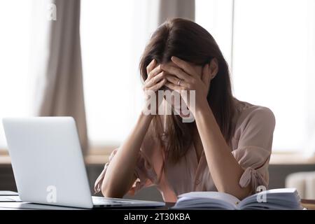Frau, die am Schreibtisch sitzt und den Kopf mit den Händen hält, fühlt sich gestresst Stockfoto