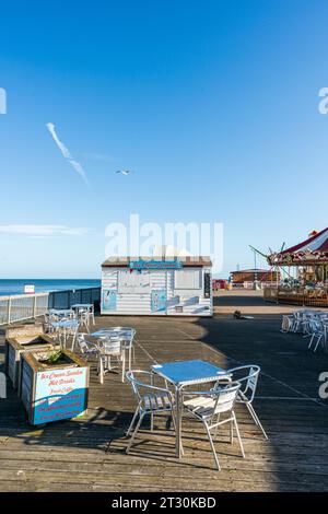 Eine verlassene Szene am Herne Bay Pier am frühen Morgen. Silberne Tische und Stühle mit einer geschlossenen weißen Holzhütte mit dem Schild „Ice Cream Sundae“. Stockfoto