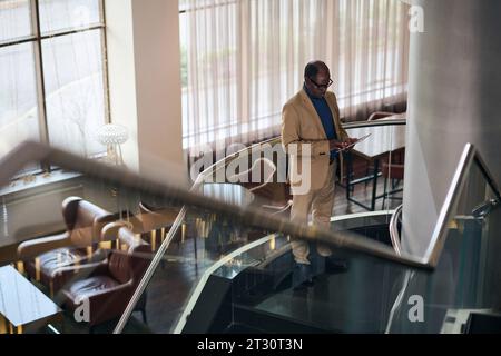 Hochwinkelansicht eines Geschäftsmannes mit Tablet-pc, während er auf der Treppe in der Lobby des Hotels steht Stockfoto