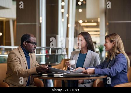 Geschäftskollegen, die sich im Hotel treffen, sitzen am Tisch und diskutieren im Team über Arbeitsmomente Stockfoto