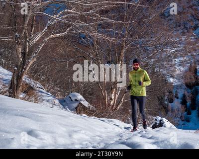 Ein männlicher Sportler trainiert im Winter in den Bergen. Ein bärtiger Kerl joggt. Trailrunning Stockfoto
