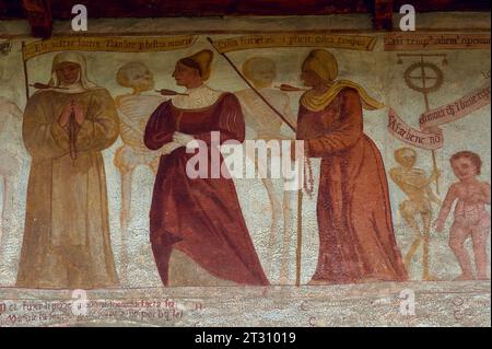 Detail aus dem 16. Jahrhundert Danza Macabra (Tanz des Todes) Freskenfries: Skelette stehen mit Nonne (links), Frau von edler Geburt (Mitte) und ältere Frau auf Stock gestützt, jede Frau durchbohrt von Pfeil des Todes. Gemalt von der italienischen Künstlerin Simone II. Baschenis (ca. 1495–1555) an der Außenwand der Chiesa di San Vigil in Pinzolo, Trentino-Südtirol, Italien. Der Fries hat Unterschriften in lokalen Dialekten und die von den gewöhnlichen Menschen verstandene Sprache. Stockfoto